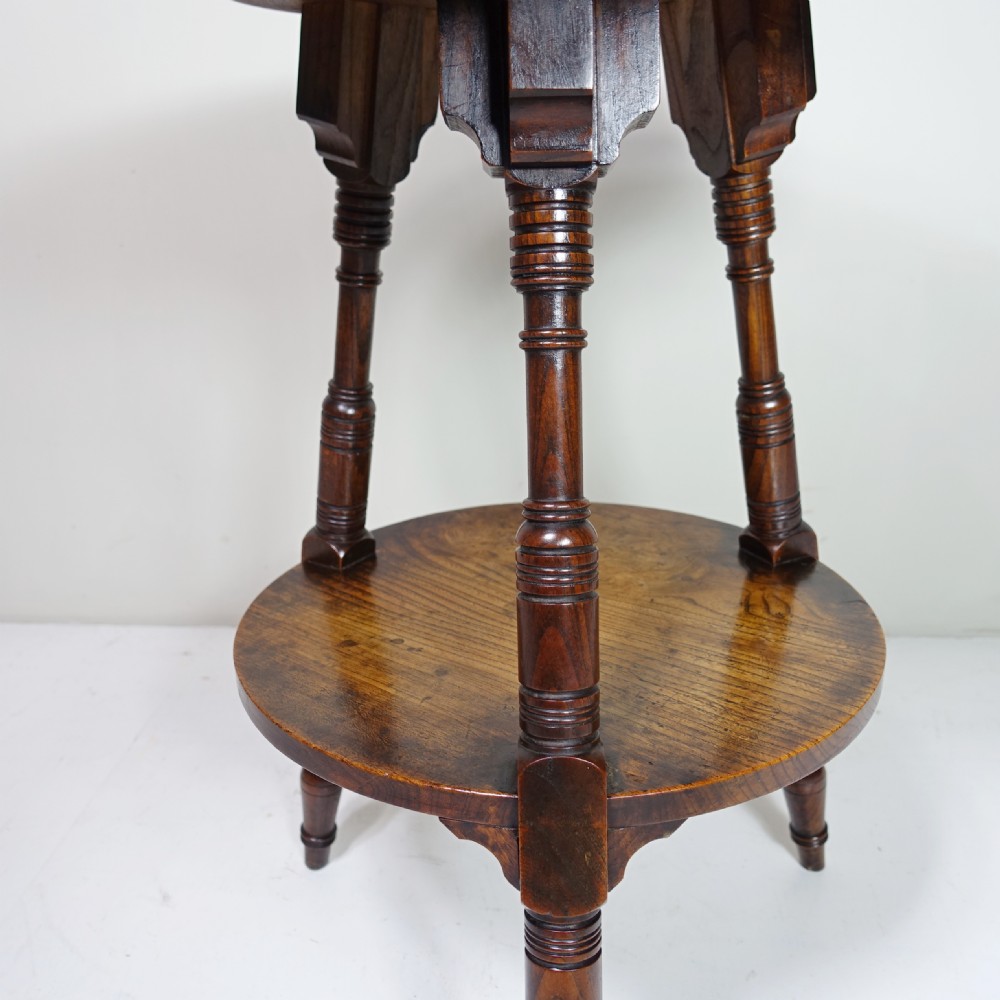 A 19th-century dark elm circular cricket table with three turned legs, decorative top brackets, and a round lower undertier shelf. View III