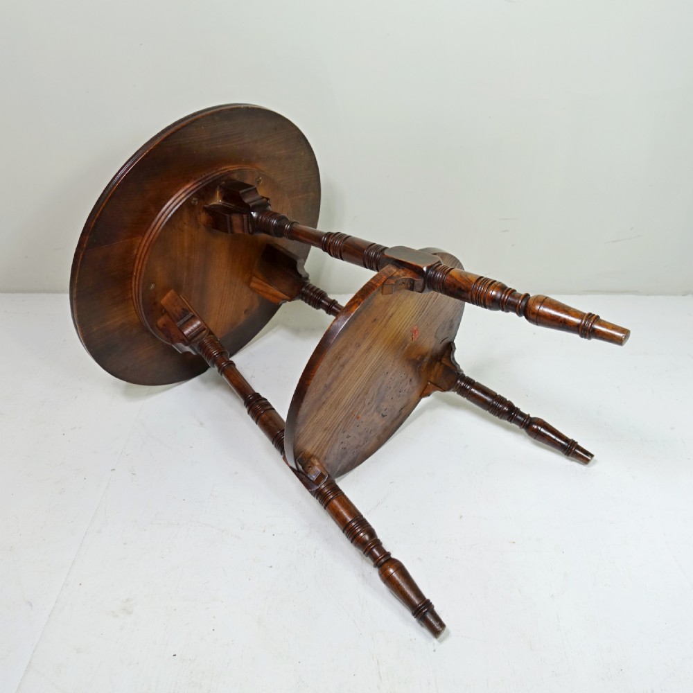 A 19th-century dark elm circular cricket table with three turned legs, decorative top brackets, and a round lower undertier shelf. View V