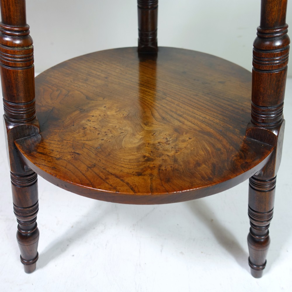 A 19th-century dark elm circular cricket table with three turned legs, decorative top brackets, and a round lower undertier shelf. View VII
