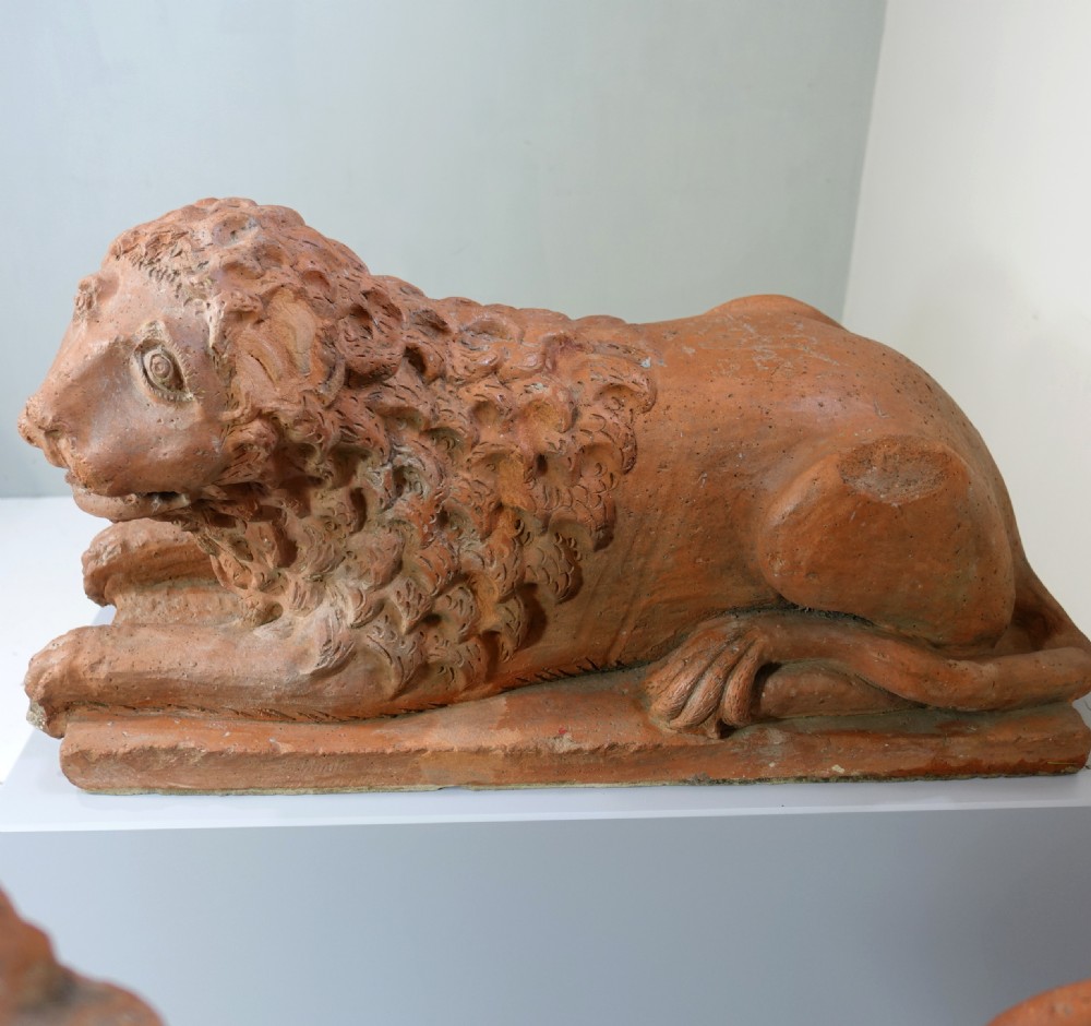 A pair of 19th-century terracotta sculptures depicting recumbent lions with textured manes, resting on integral rectangular bases. View V