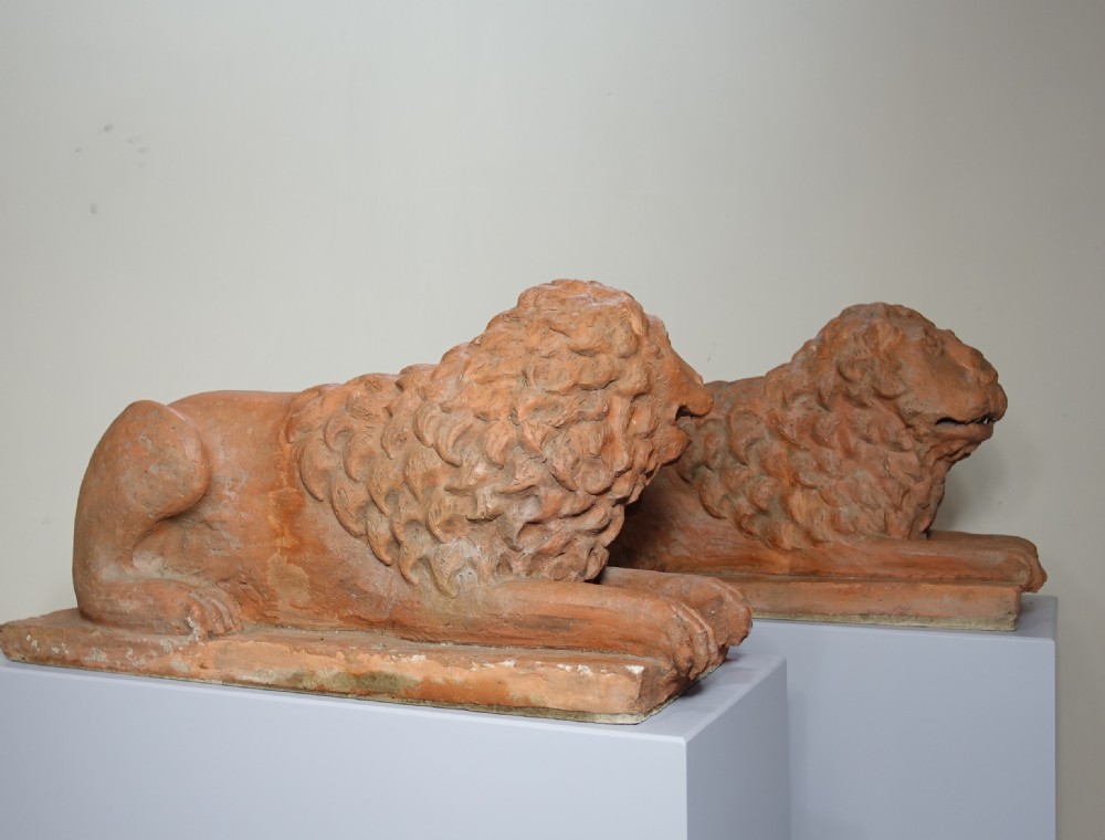 A pair of 19th-century terracotta sculptures depicting recumbent lions with textured manes, resting on integral rectangular bases. View VI