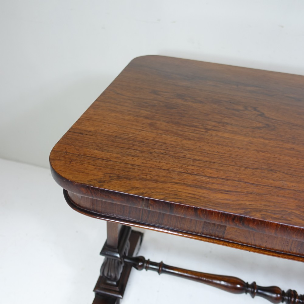 A William IV dark rosewood table featuring a rectangular top with rounded corners, supported by carved dual pedestal legs connected by a central turned stretcher. View III