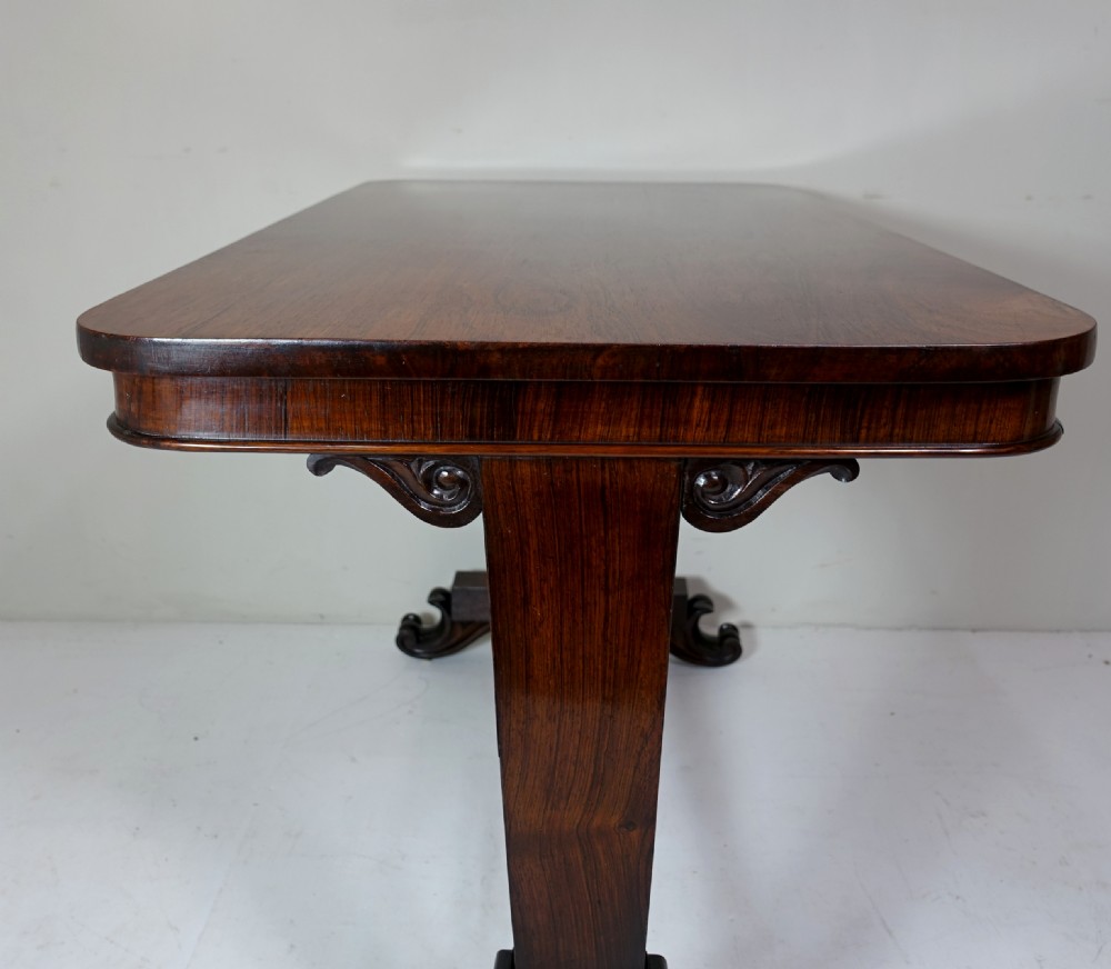 A William IV dark rosewood table featuring a rectangular top with rounded corners, supported by carved dual pedestal legs connected by a central turned stretcher. View VI