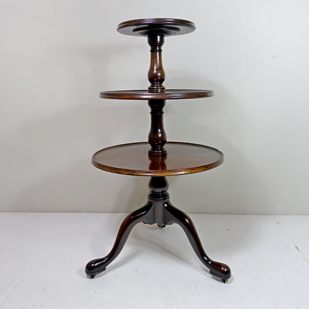 An 18th-century mahogany dumb waiter table featuring three graduated circular tiers supported by turned columns on a tripod base with castors. View VI