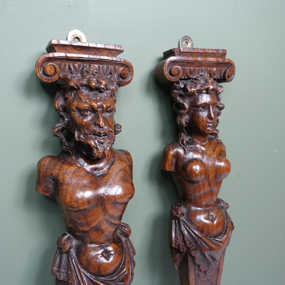 A pair of early nineteenth-century carved chestnut herms depicting male and female busts with Ionic scroll capitals above tapered, scale-carved bases. View V