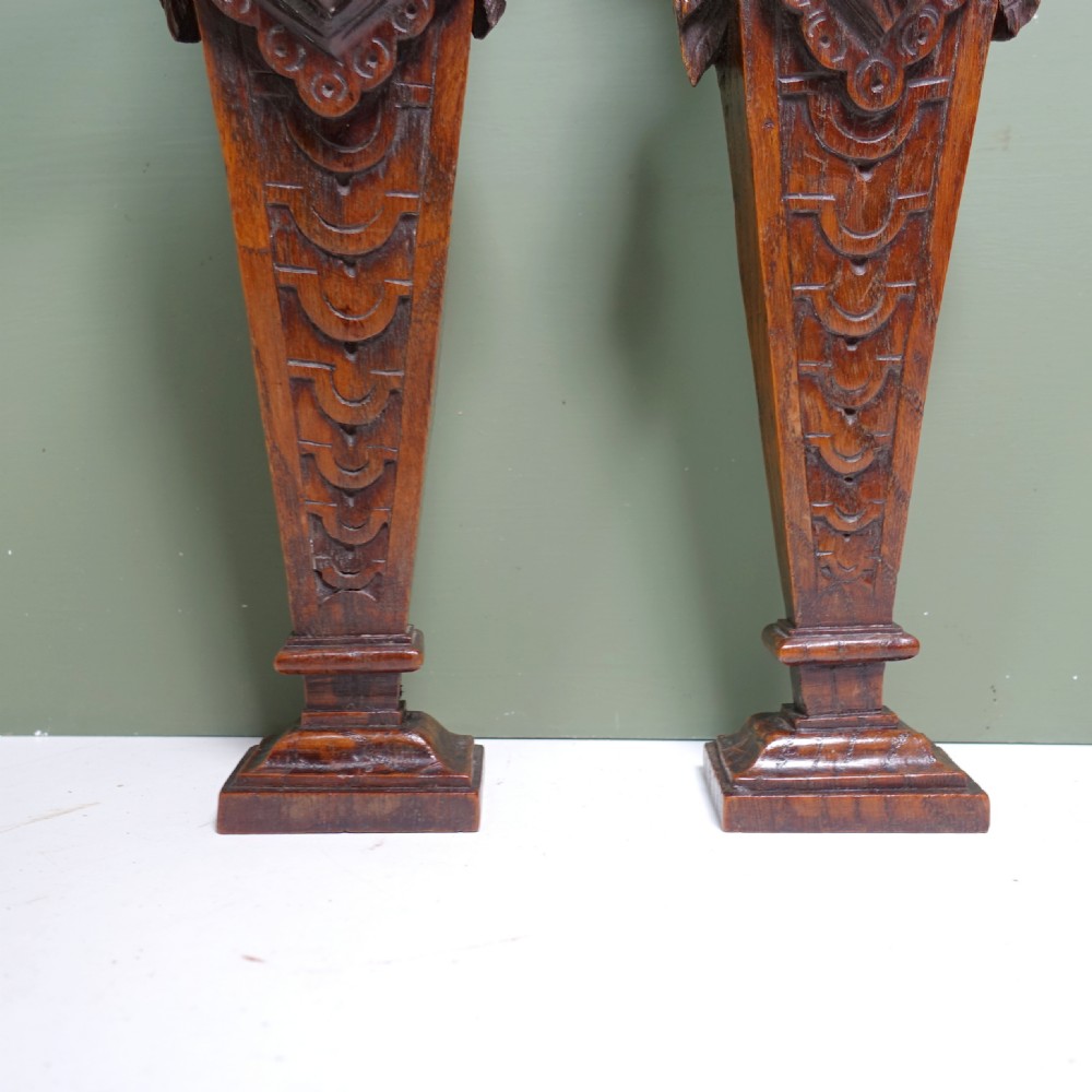 A pair of early nineteenth-century carved chestnut herms depicting male and female busts with Ionic scroll capitals above tapered, scale-carved bases. View VI