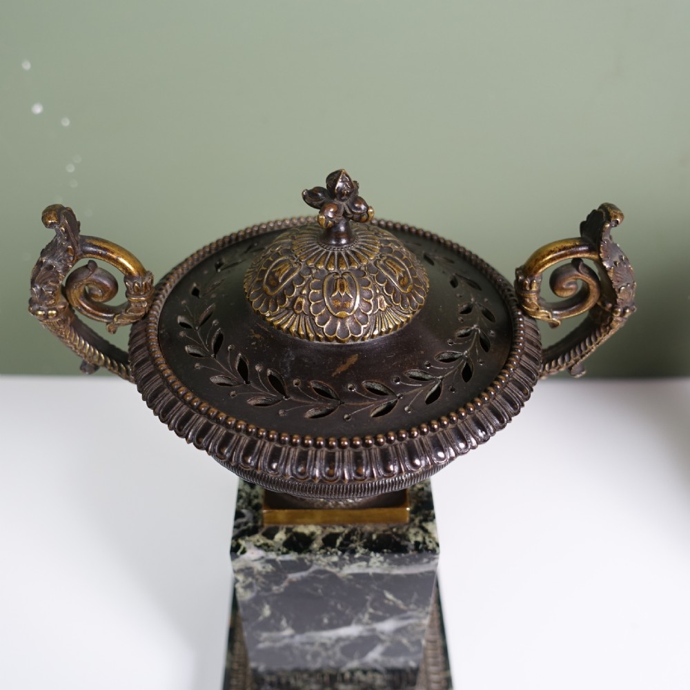 A pair of early 19th-century patinated bronze urns with gilt scroll handles, raised on dark green marble plinths. View V
