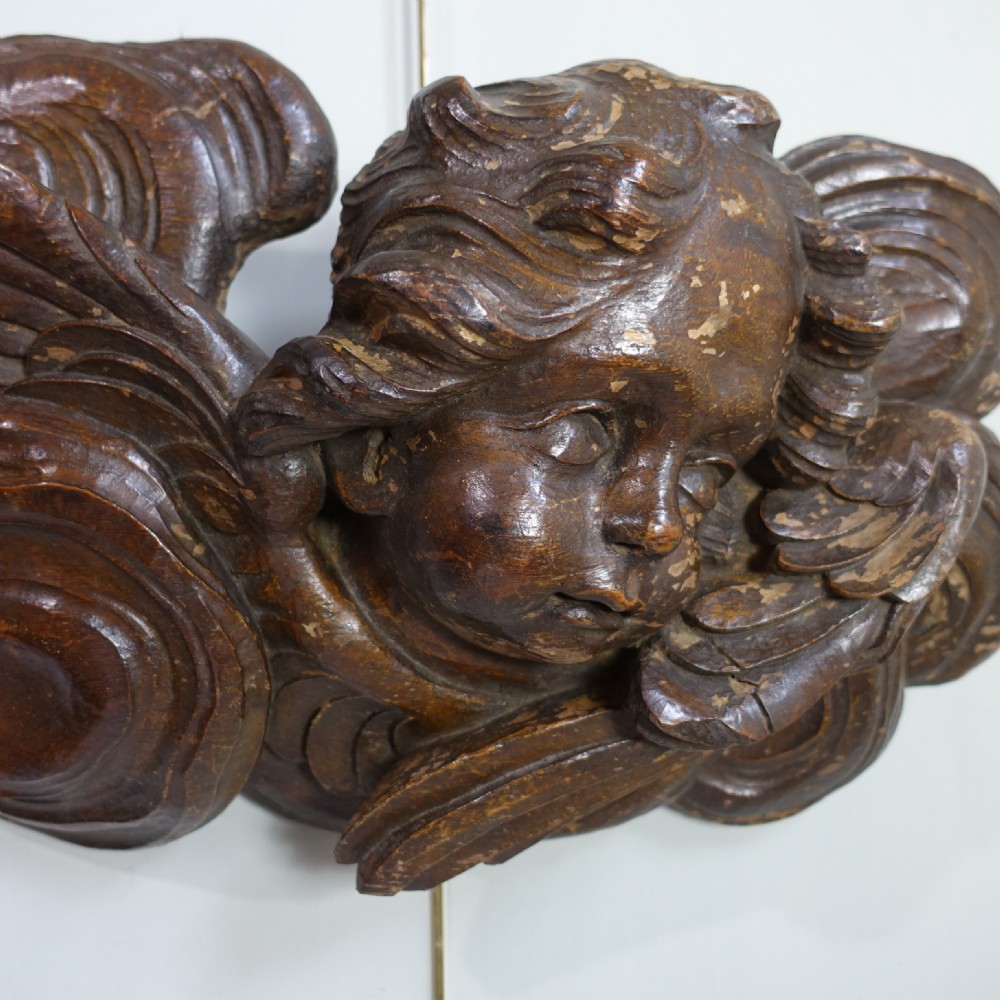A dark oak Baroque relief carving featuring a winged cherub head surrounded by carved cloud motifs. View II