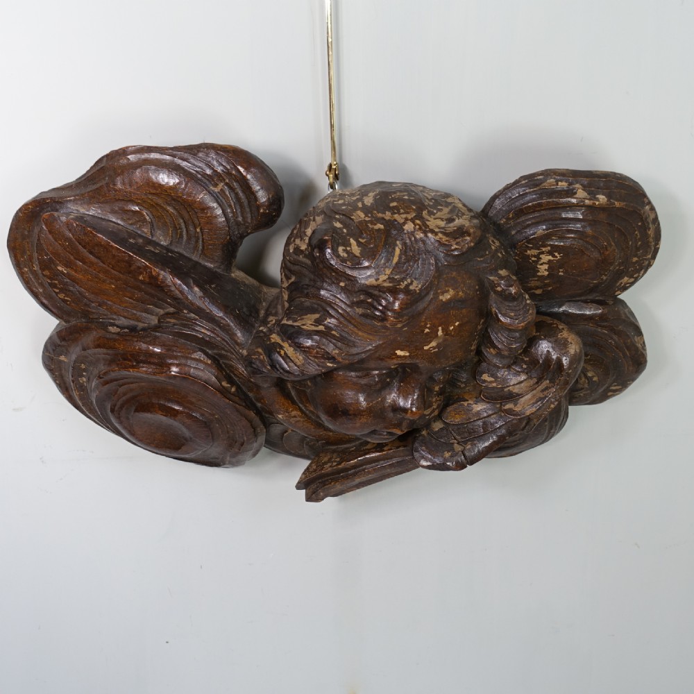 A dark oak Baroque relief carving featuring a winged cherub head surrounded by carved cloud motifs. View III