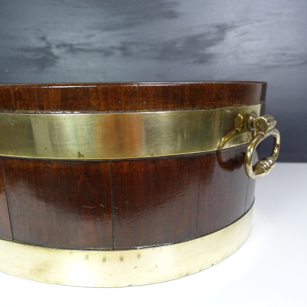 An eighteenth-century oval mahogany wine cooler featuring two wide brass bands around the exterior body and brass drop ring handles on each side. View III