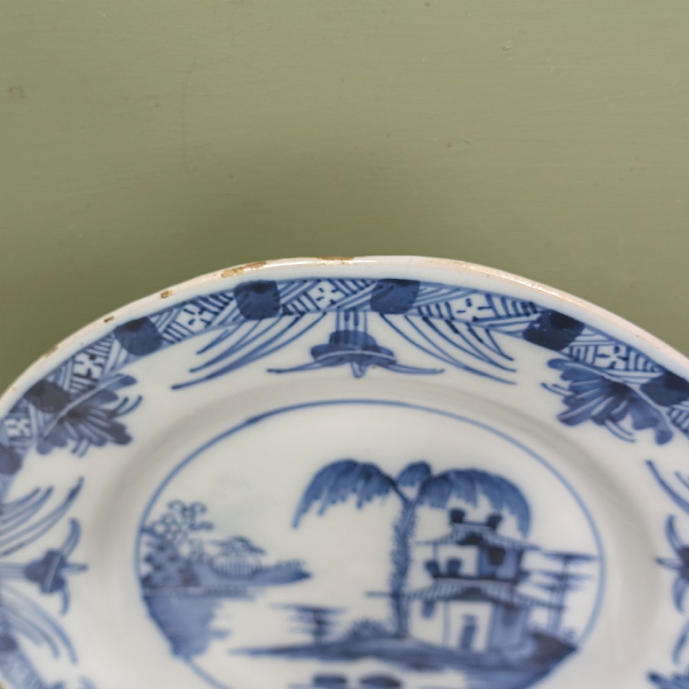 A set of four 18th-century tin-glazed earthenware delft plates, hand-painted in cobalt blue with chinoiserie pagoda landscapes and decorative rims on a pale ground. View VI