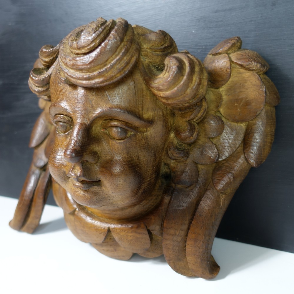 An 18th-century hand-carved oak relief sculpture depicting a cherub head with winged detail and curly hair. View III
