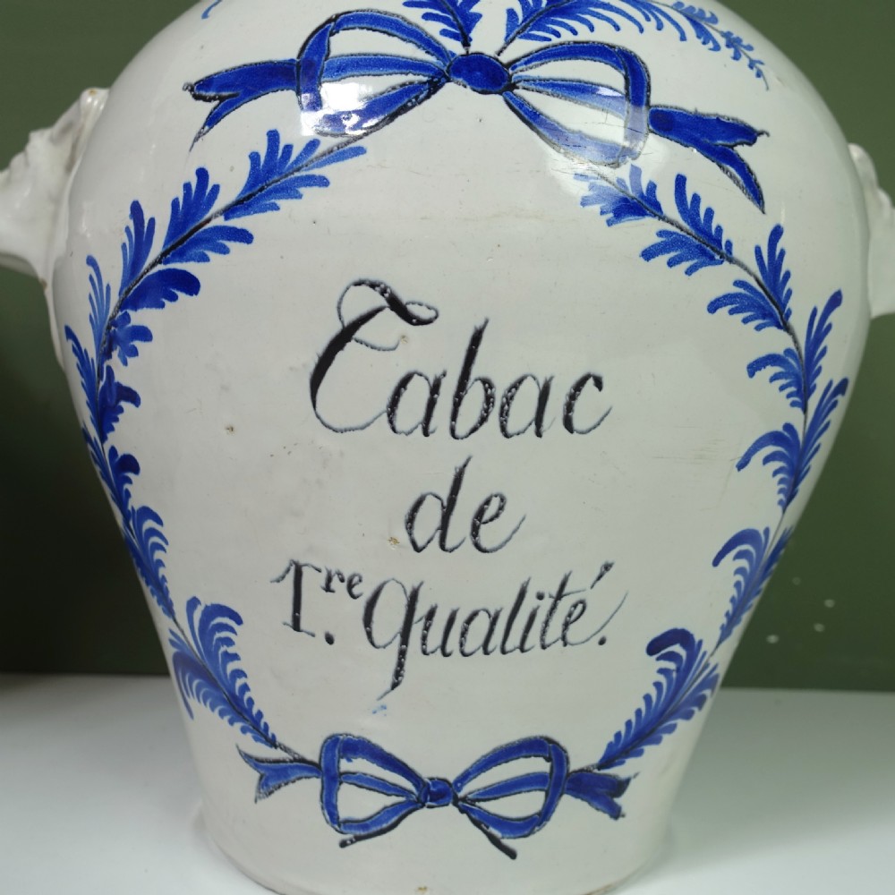A pair of 18th-century white tin-glazed earthenware tobacco jars featuring blue hand-painted wreaths, inscriptions, molded handles, and stepped brass lids. View VII