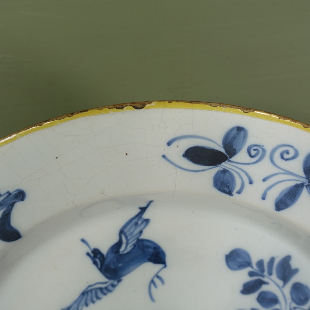 An 18th-century tin-glazed earthenware Delft charger featuring hand-painted cobalt blue floral motifs, a flying bird, and a yellow rim. View II