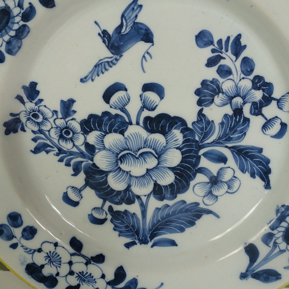 An 18th-century tin-glazed earthenware Delft charger featuring hand-painted cobalt blue floral motifs, a flying bird, and a yellow rim. View III
