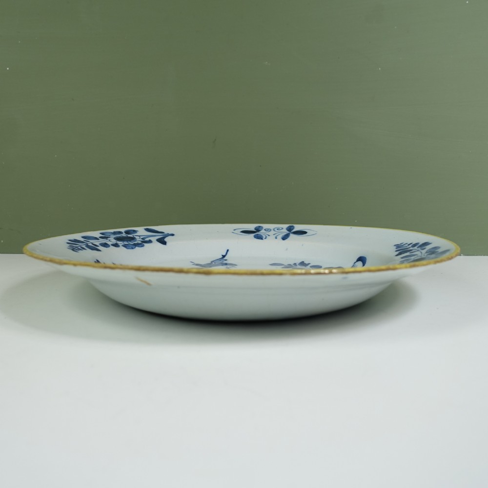 An 18th-century tin-glazed earthenware Delft charger featuring hand-painted cobalt blue floral motifs, a flying bird, and a yellow rim. View V
