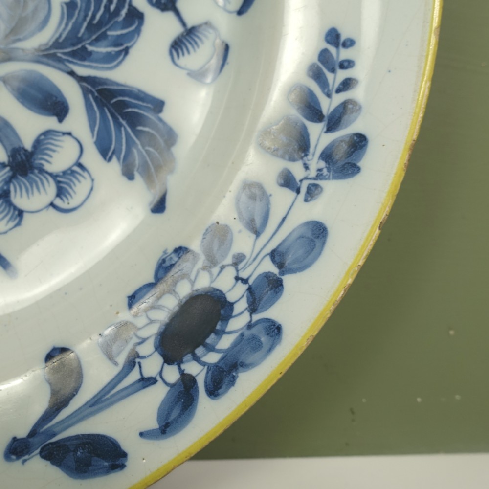 An 18th-century tin-glazed earthenware Delft charger featuring hand-painted cobalt blue floral motifs, a flying bird, and a yellow rim. View VII