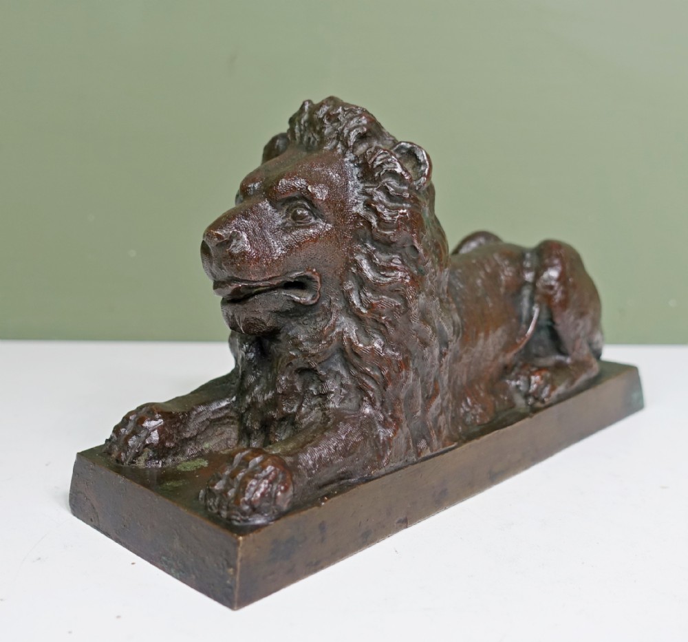 An early nineteenth-century cast bronze sculpture depicting a recumbent lion on a rectangular plinth base with a dark patinated finish.