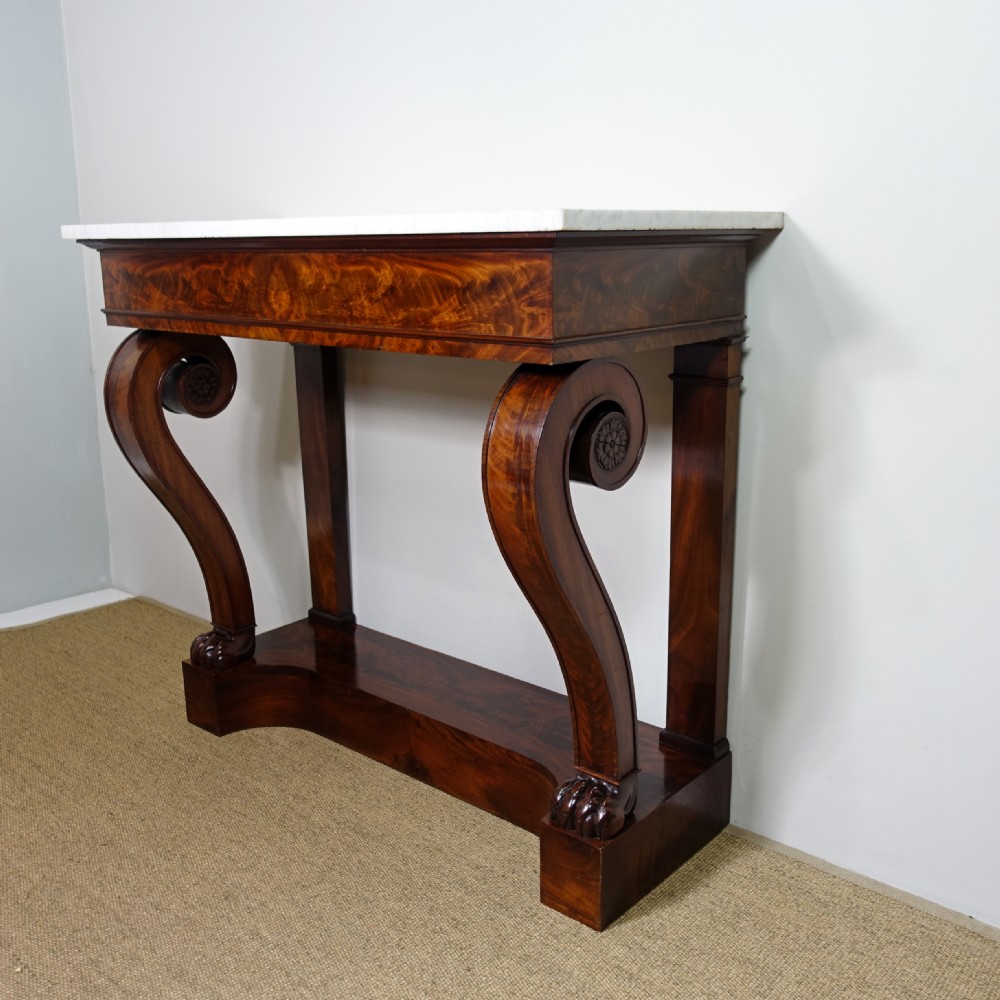 A 19th-century mahogany console table featuring a white marble top, scrolled front supports terminating in carved paw feet, flame mahogany veneer, and a plinth base. View II