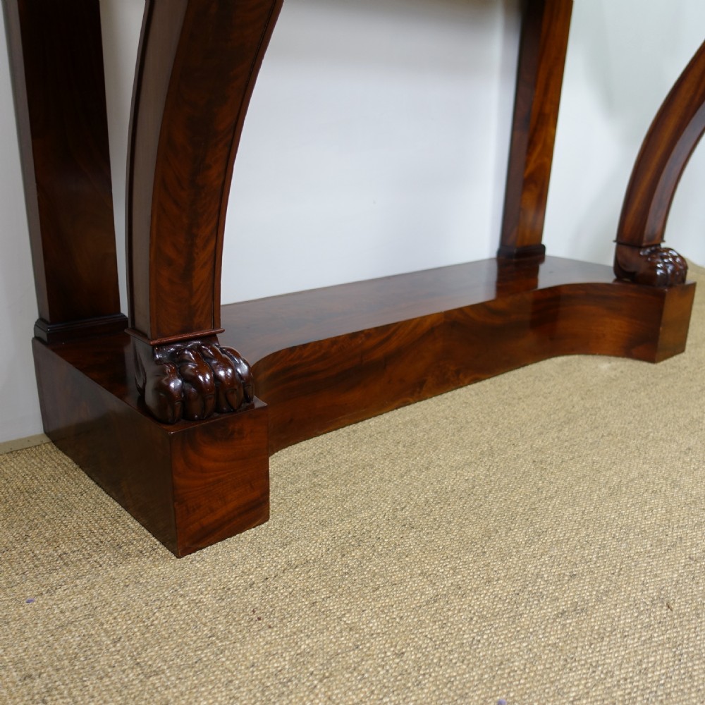 A 19th-century mahogany console table featuring a white marble top, scrolled front supports terminating in carved paw feet, flame mahogany veneer, and a plinth base. View VI