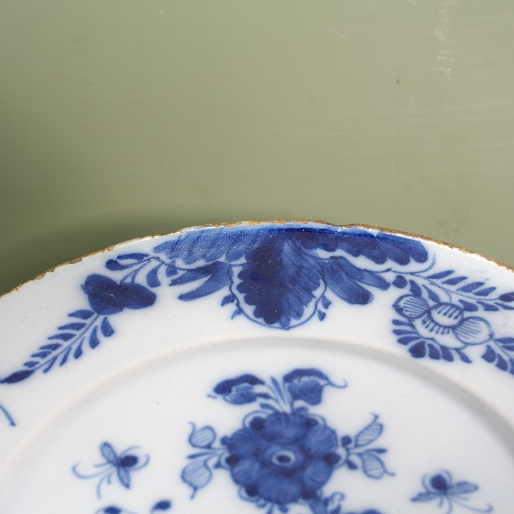An 18th-century circular tin-glazed earthenware charger plate featuring hand-painted cobalt blue floral motifs and an ornate patterned rim. View VI