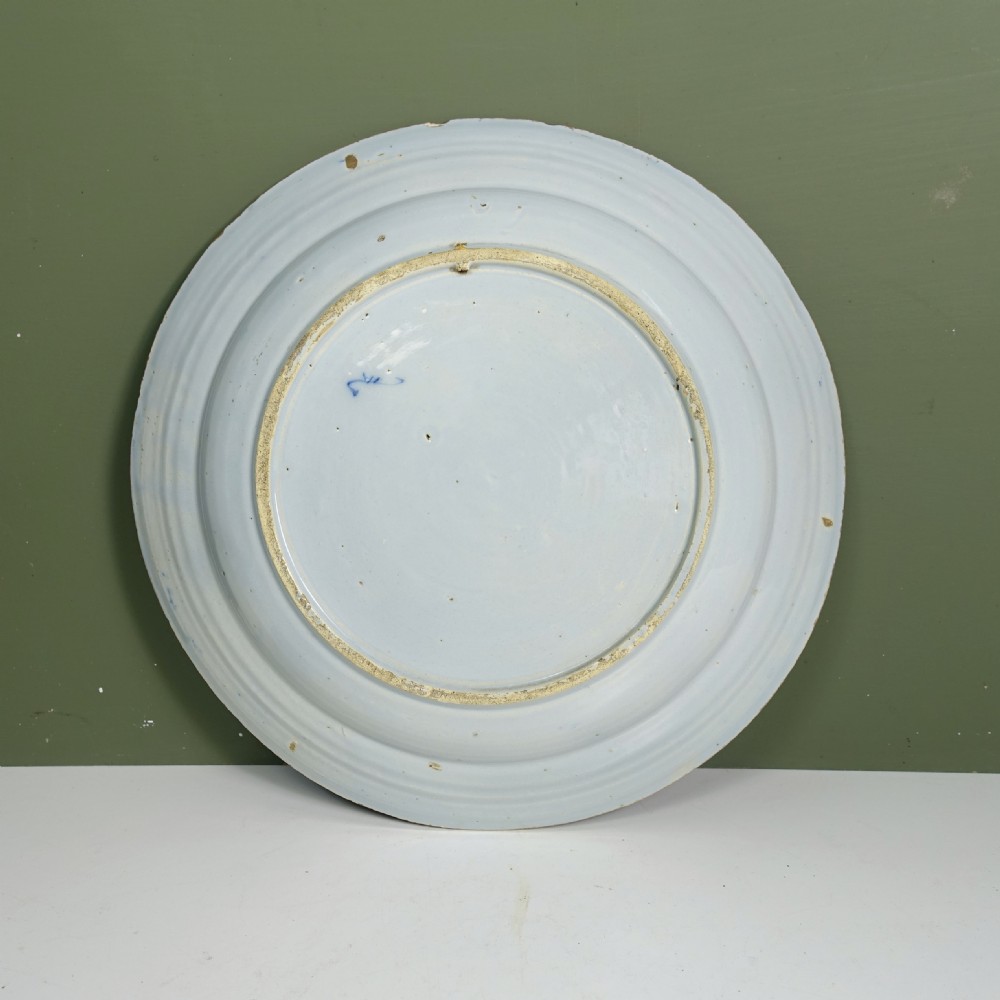 An 18th-century circular tin-glazed earthenware charger plate featuring hand-painted cobalt blue floral motifs and an ornate patterned rim. View VII