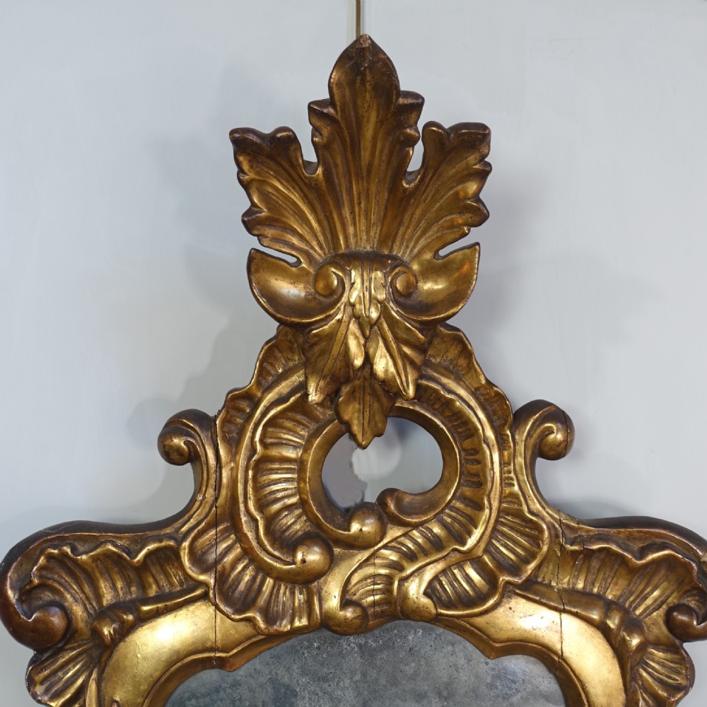 An 18th-century carved giltwood wall mirror featuring elaborate scrolling acanthus leaves, a central crest, and foxed mirror glass. View III