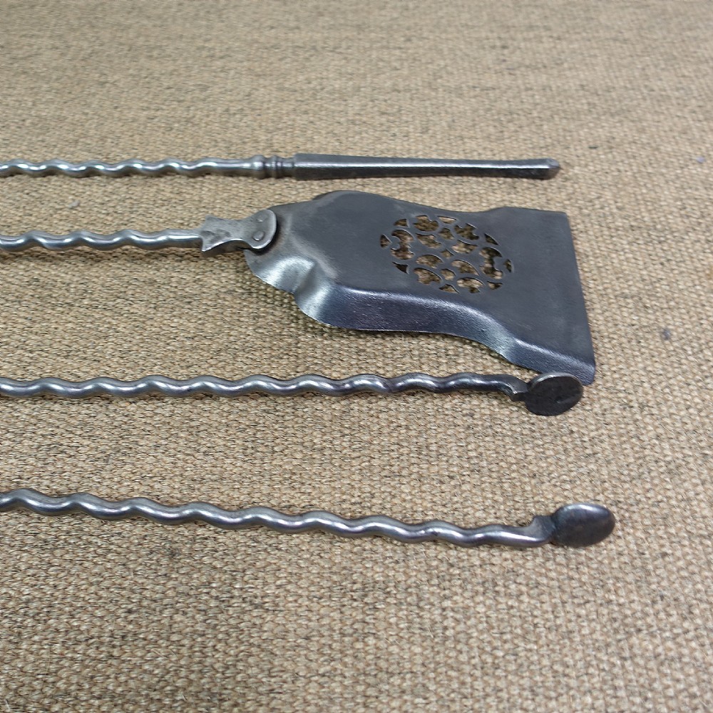 A set of three early 19th-century burnished steel fire tools including tongs, a poker, and a shovel with a pierced pattern and spiralled handles. View IV