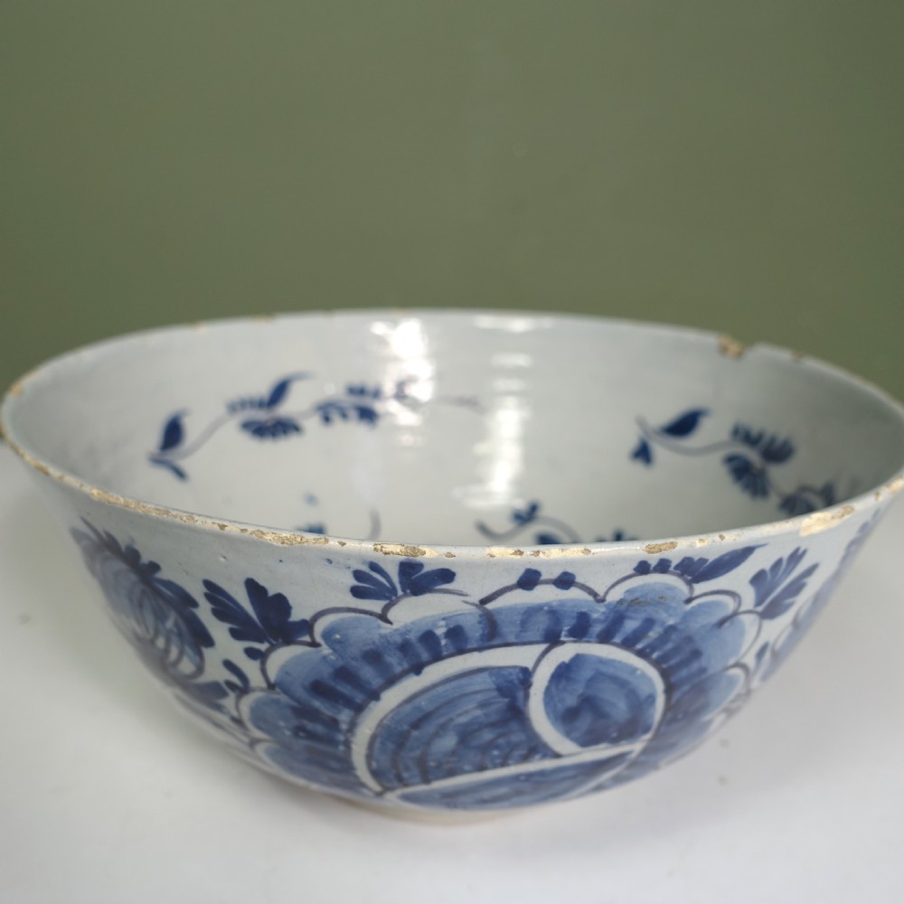 An 18th-century round tin-glazed earthenware bowl featuring hand-painted cobalt blue floral motifs on a white background with minor glaze chipping along the rim. View VI