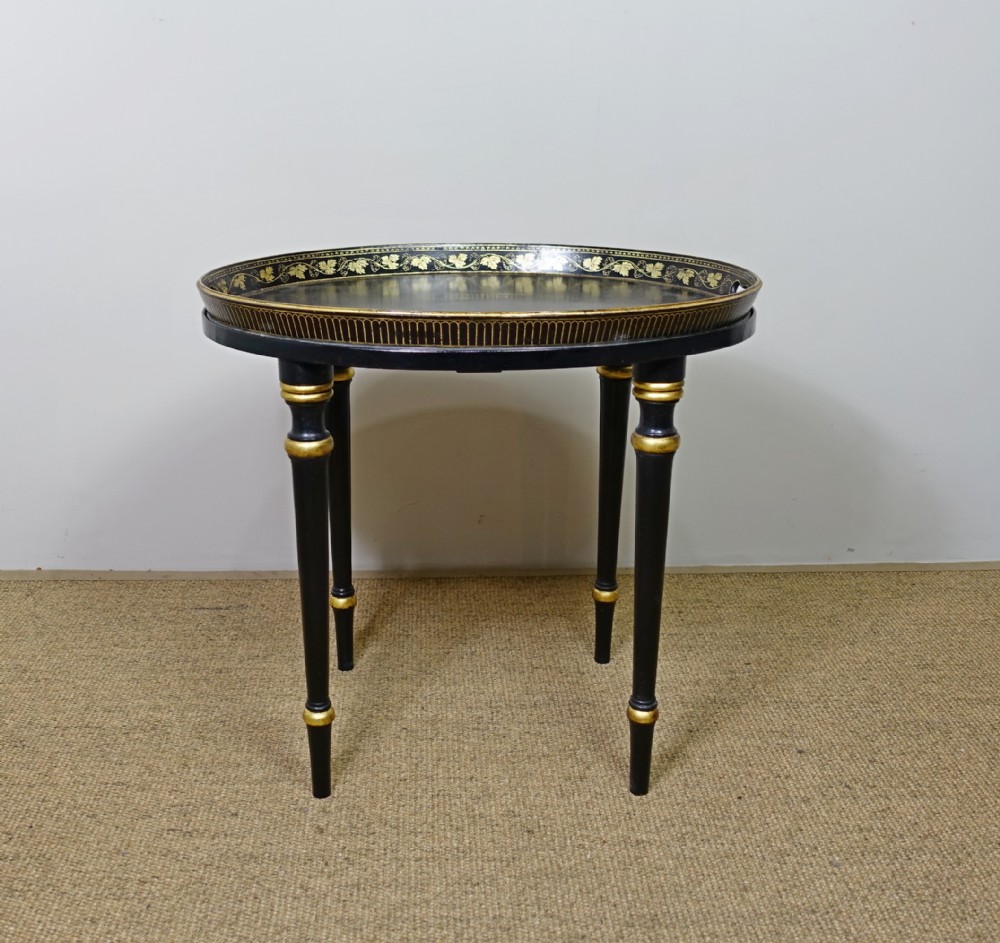 An oval black papier-mache tray with gilded leaf borders mounted on a black turned wood stand with gold accents.