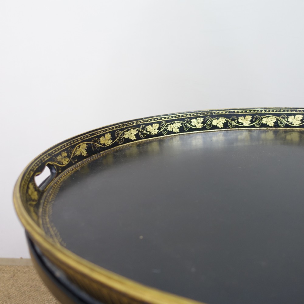 An oval black papier-mache tray with gilded leaf borders mounted on a black turned wood stand with gold accents. View V