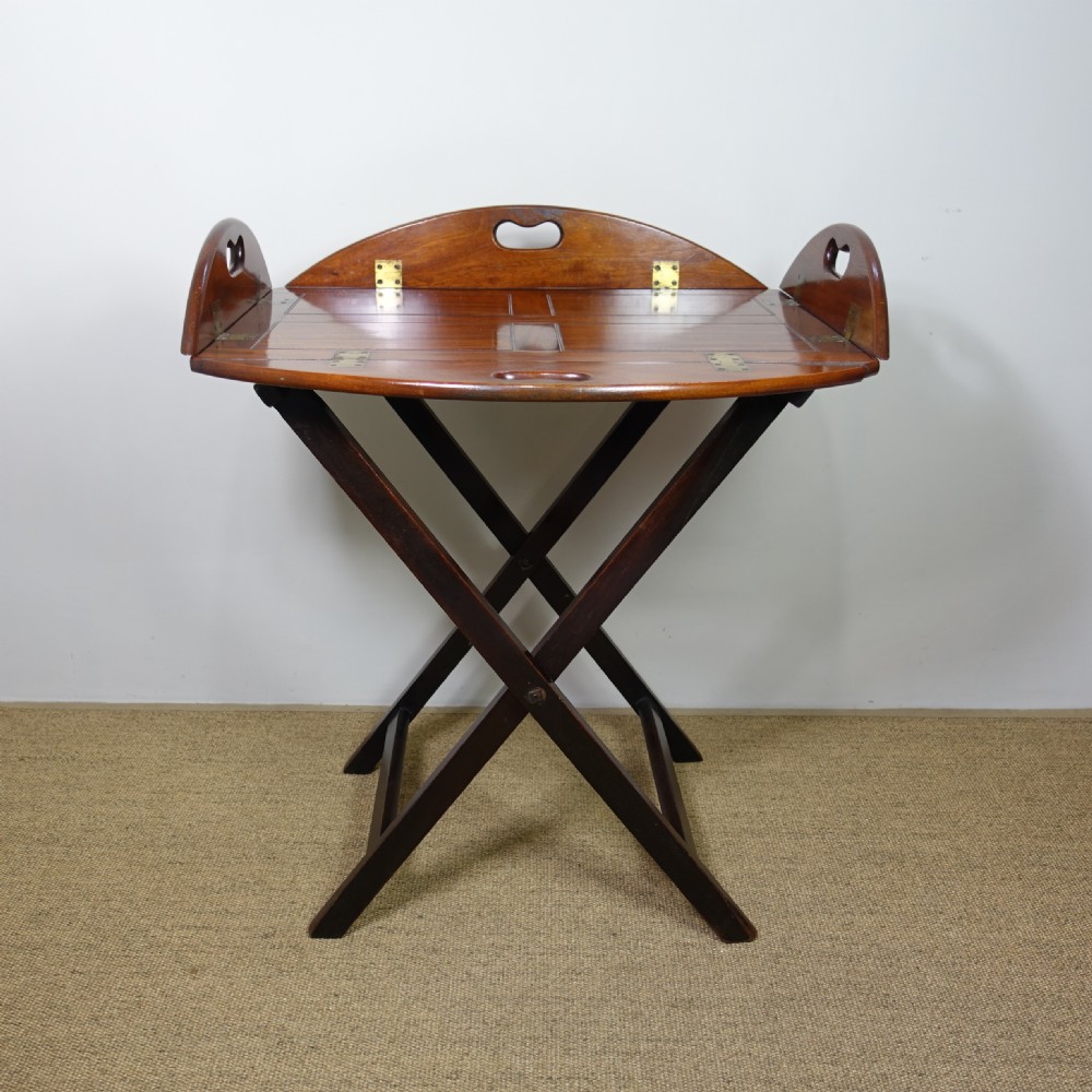 A George III mahogany butlers tray with hinged gallery sides resting on a folding cross-frame stand.