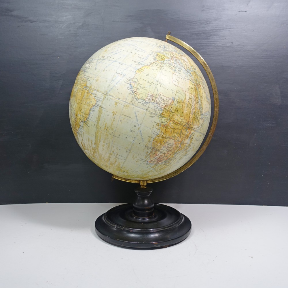 A vintage terrestrial globe featuring printed paper maps on a brass semi-meridian arc, mounted to a dark circular turned wooden base.