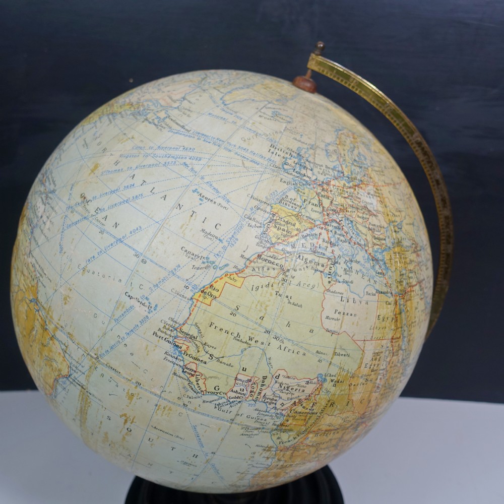 A vintage terrestrial globe featuring printed paper maps on a brass semi-meridian arc, mounted to a dark circular turned wooden base. View IV