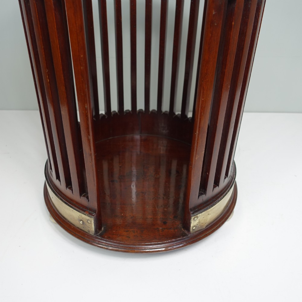 A circular Georgian mahogany slatted plate bucket with brass bound rim and base, a brass swing handle, and a cut-out front opening containing dinner plates. View II