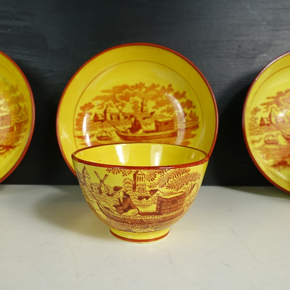 Eight yellow earthenware tea bowls with matching saucers decorated in reddish-brown printed pastoral landscapes. View V