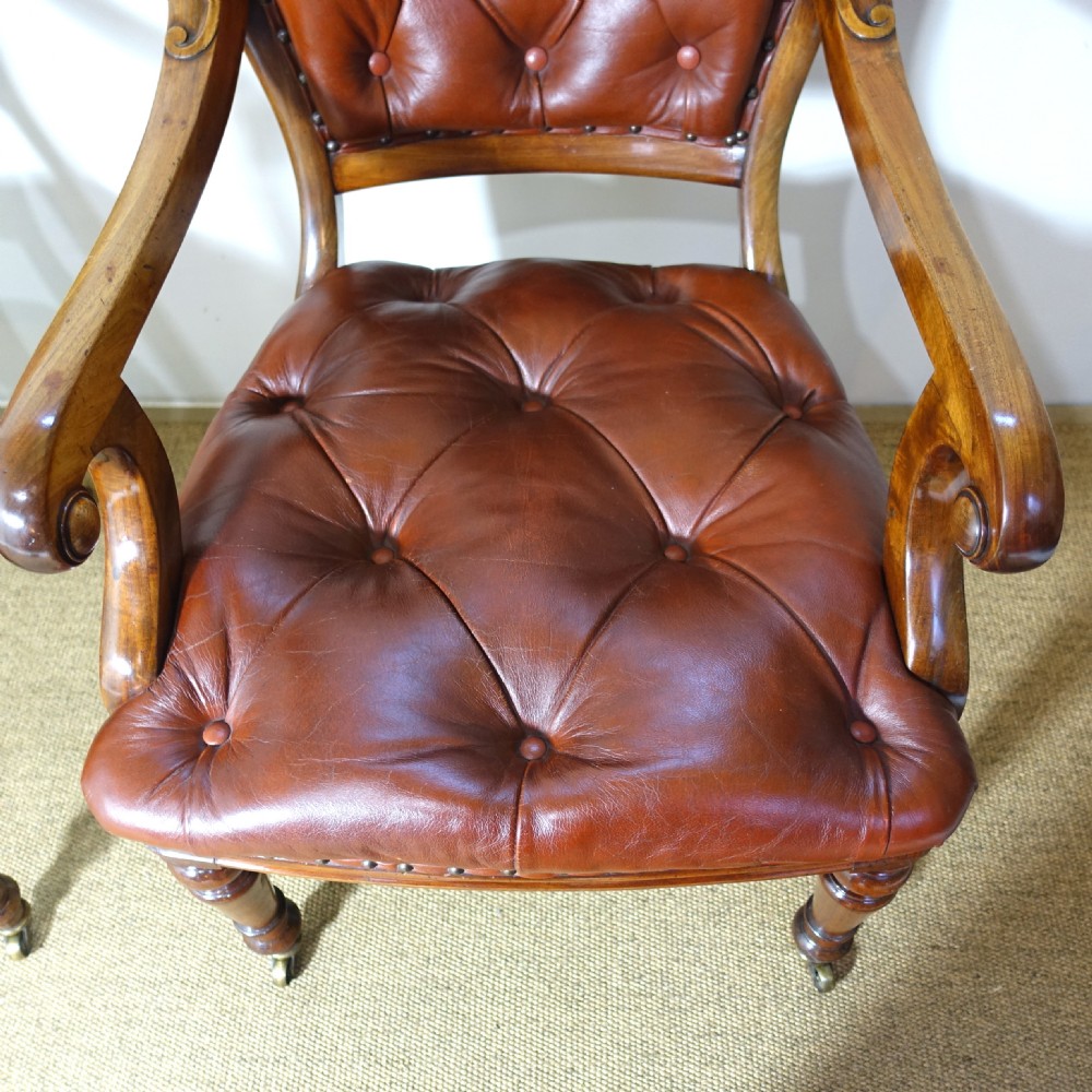 A pair of 19th-century mahogany armchairs upholstered in deep-buttoned reddish-brown leather with brass stud detail and turned front legs on castors. View V