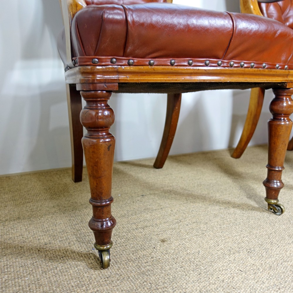 A pair of 19th-century mahogany armchairs upholstered in deep-buttoned reddish-brown leather with brass stud detail and turned front legs on castors. View VI