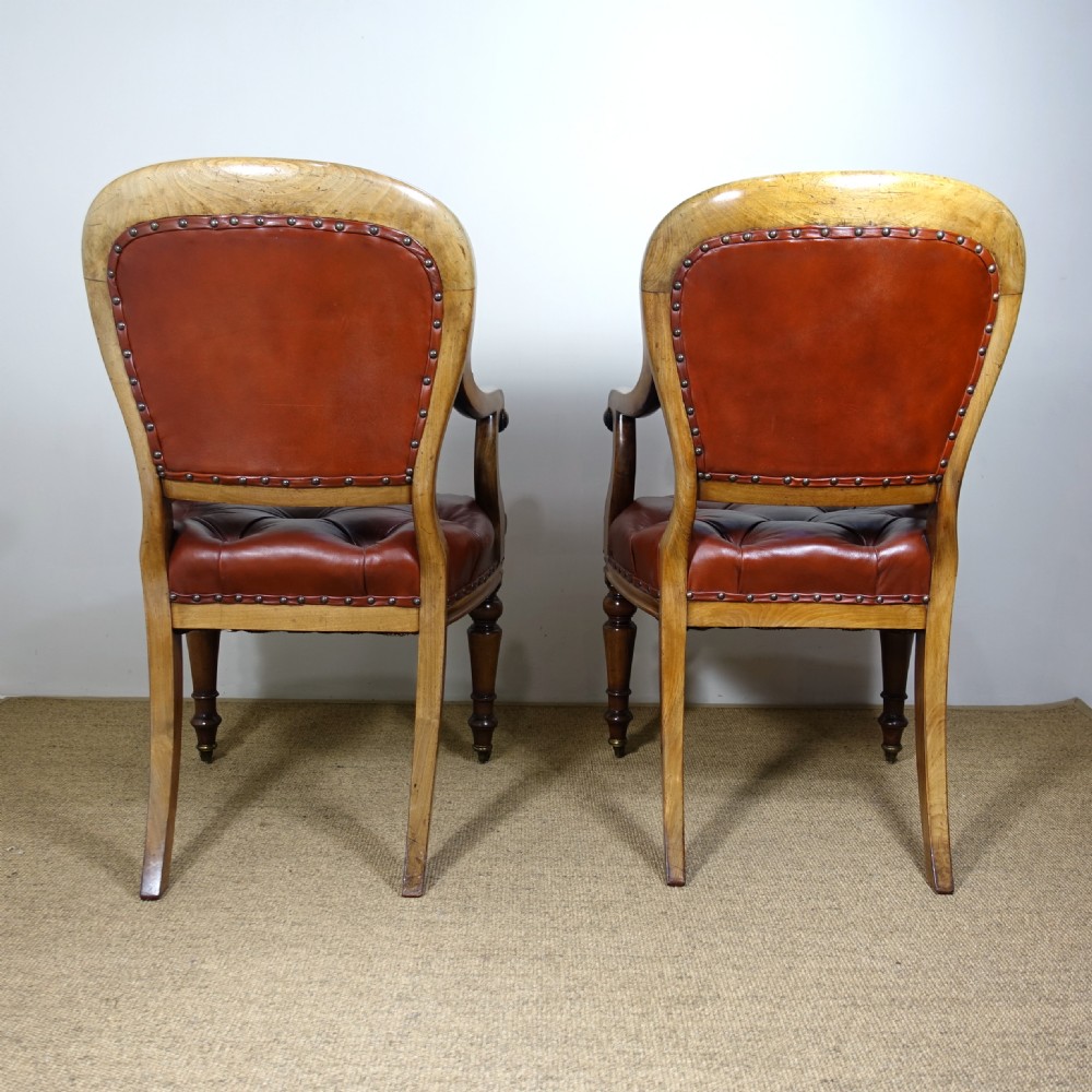 A pair of 19th-century mahogany armchairs upholstered in deep-buttoned reddish-brown leather with brass stud detail and turned front legs on castors. View VII