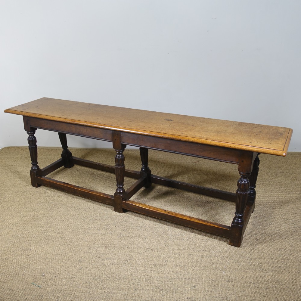 A long 19th-century dark oak stool featuring a flat plank top supported by six turned legs and low perimeter stretchers. View II