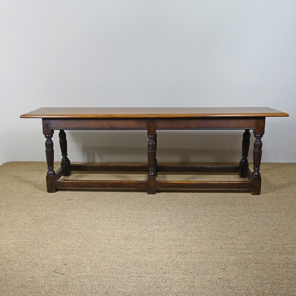A long 19th-century dark oak stool featuring a flat plank top supported by six turned legs and low perimeter stretchers. View III