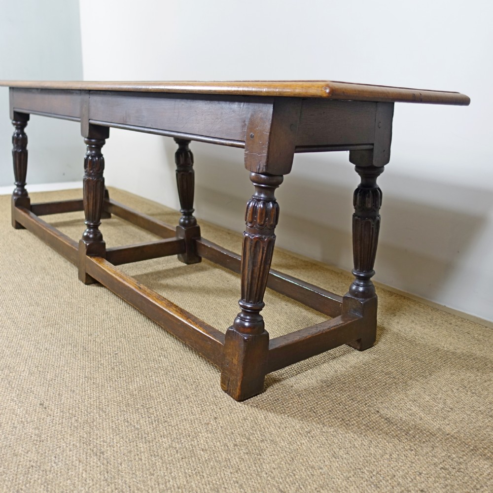 A long 19th-century dark oak stool featuring a flat plank top supported by six turned legs and low perimeter stretchers. View IV