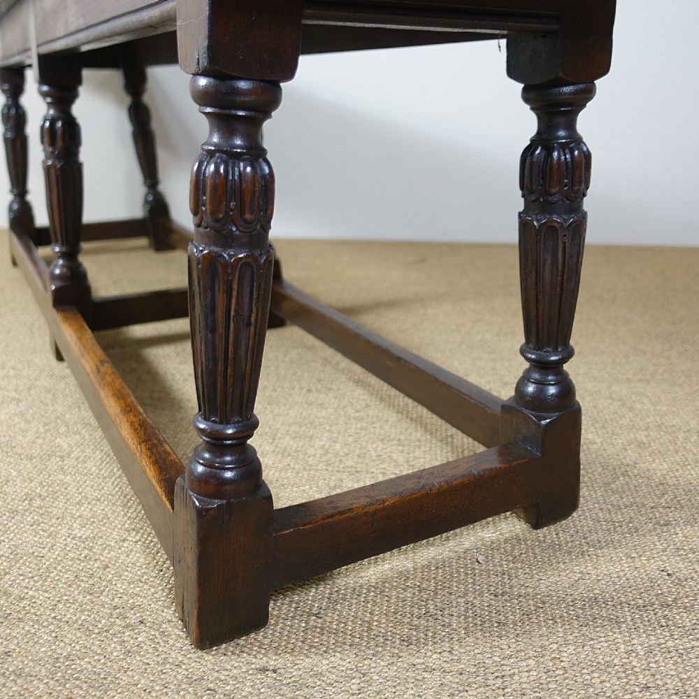 A long 19th-century dark oak stool featuring a flat plank top supported by six turned legs and low perimeter stretchers. View VI