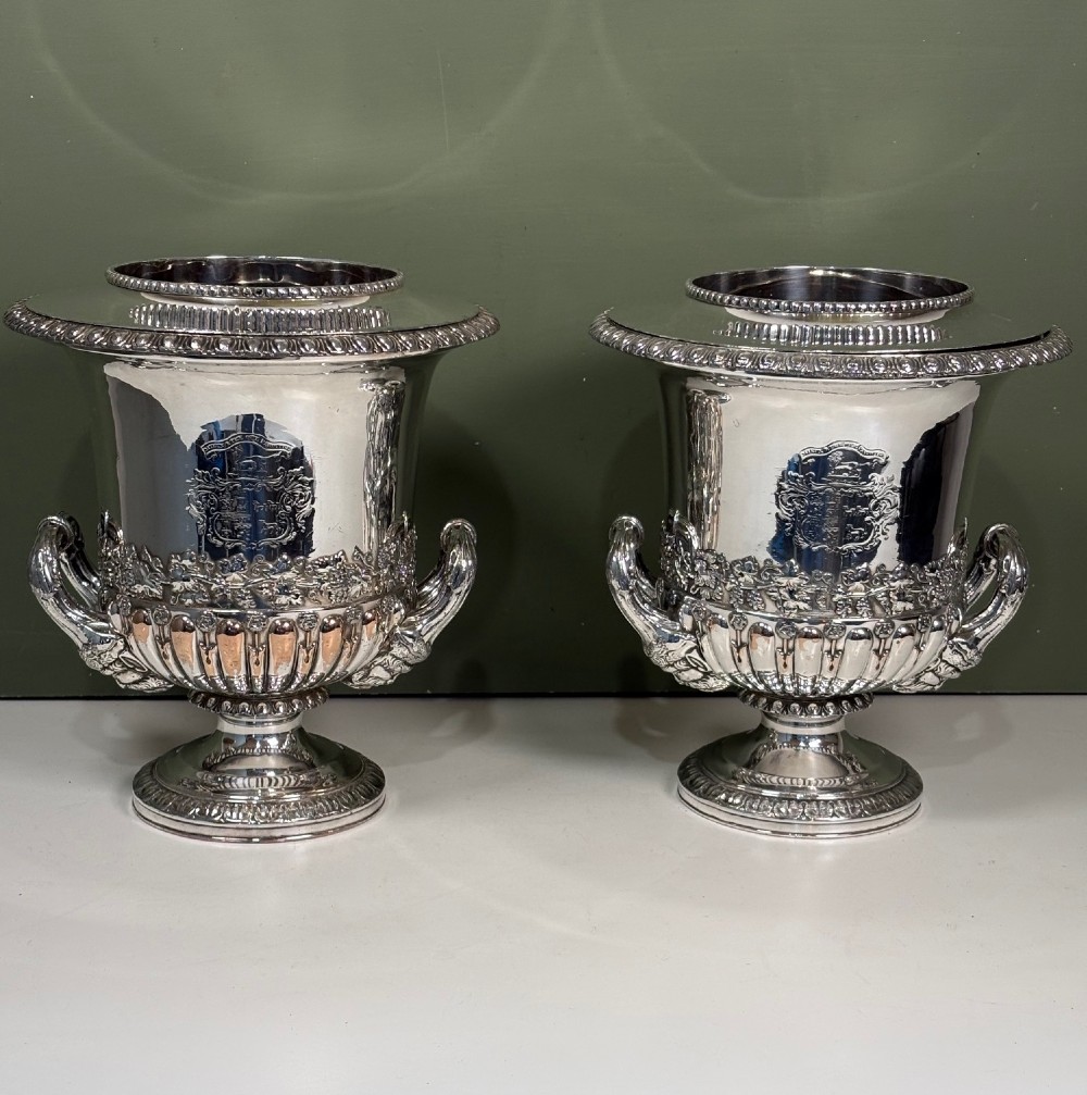 A pair of 19th-century silver-plated urn-shaped wine coolers featuring engraved crests, double scroll handles, fluted bases, and removable liners.