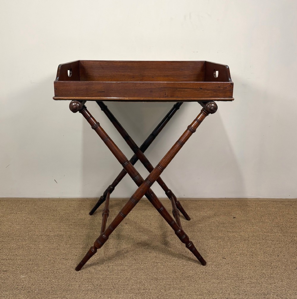 A 19th-century mahogany butlers tray with cut-out handles resting on a turned folding X-frame stand.