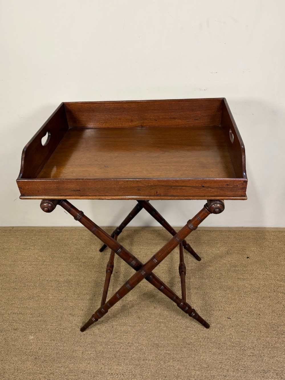A 19th-century mahogany butlers tray with cut-out handles resting on a turned folding X-frame stand. View II