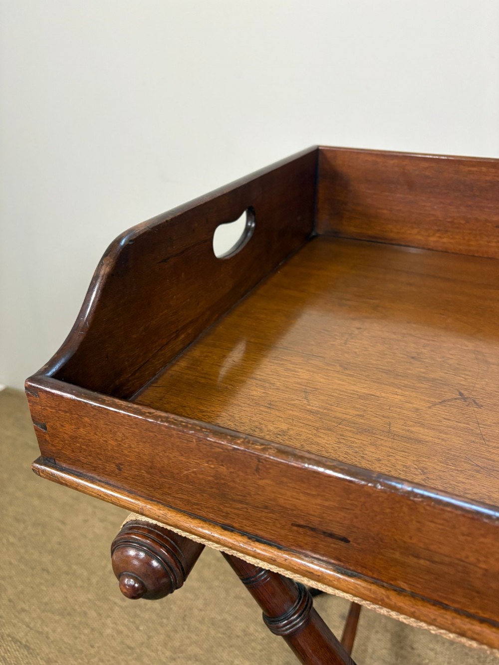 A 19th-century mahogany butlers tray with cut-out handles resting on a turned folding X-frame stand. View VII