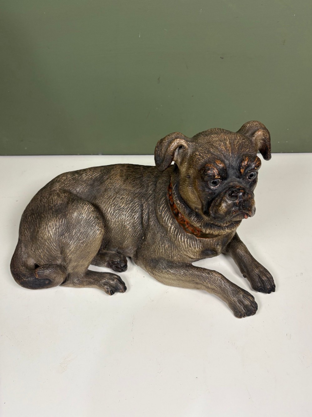A nineteenth-century ceramic figurine depicting a reclining pug dog with a textured dark brown finish and a painted collar. View II