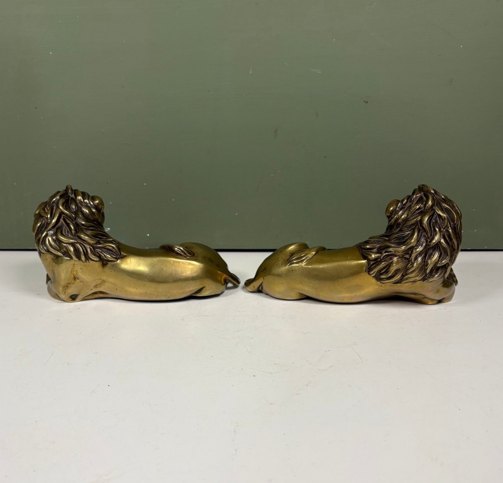 A pair of cast brass figures depicting recumbent lions with detailed manes and crossed paws facing forward. View III