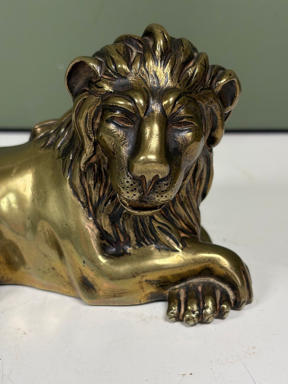 A pair of cast brass figures depicting recumbent lions with detailed manes and crossed paws facing forward. View IV